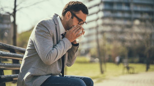 Man blowing his nose on a bench during allergy season