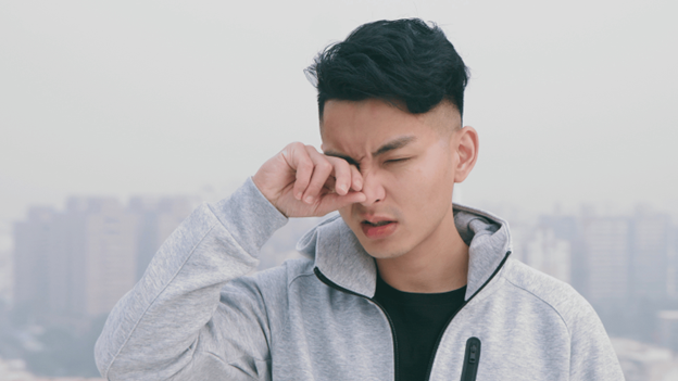 Man rubbing his irritated eye outdoors, showing common symptoms of pink eye or allergies