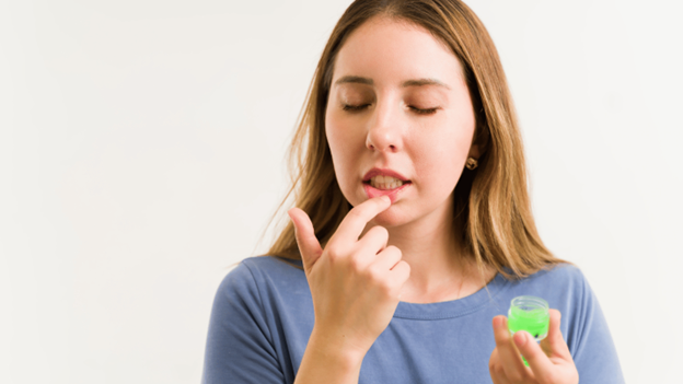 Young woman applying lip balm to a busted lip for healing and protection