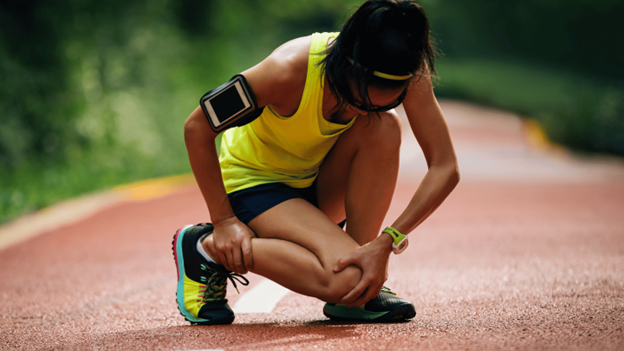 Woman athlete gripping her leg in pain due to leg cramps from overuse