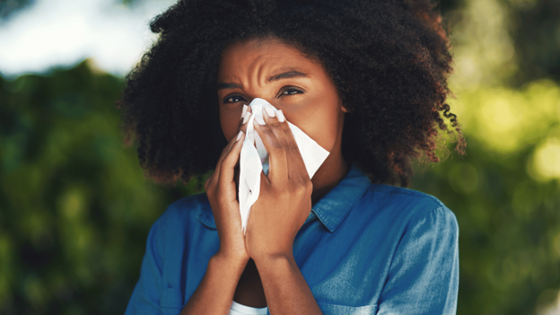 A woman blowing her nose, possibly experiencing symptoms of a summer cold or seasonal allergies