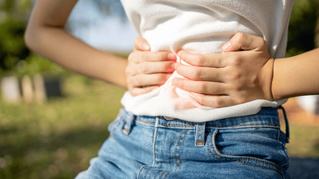 Person clutching their stomach outdoors, possibly experiencing stomach bug symptoms like cramping or abdominal pain in warm weather.