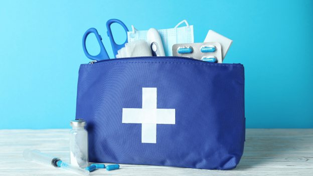 Travel medicine kit with first-aid supplies, pills, thermometer and face masks, packed in a blue bag with a white cross symbol.