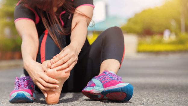 Woman in athletic wear holding her foot in pain after running, showing signs of possible foot injury or plantar fasciitis.