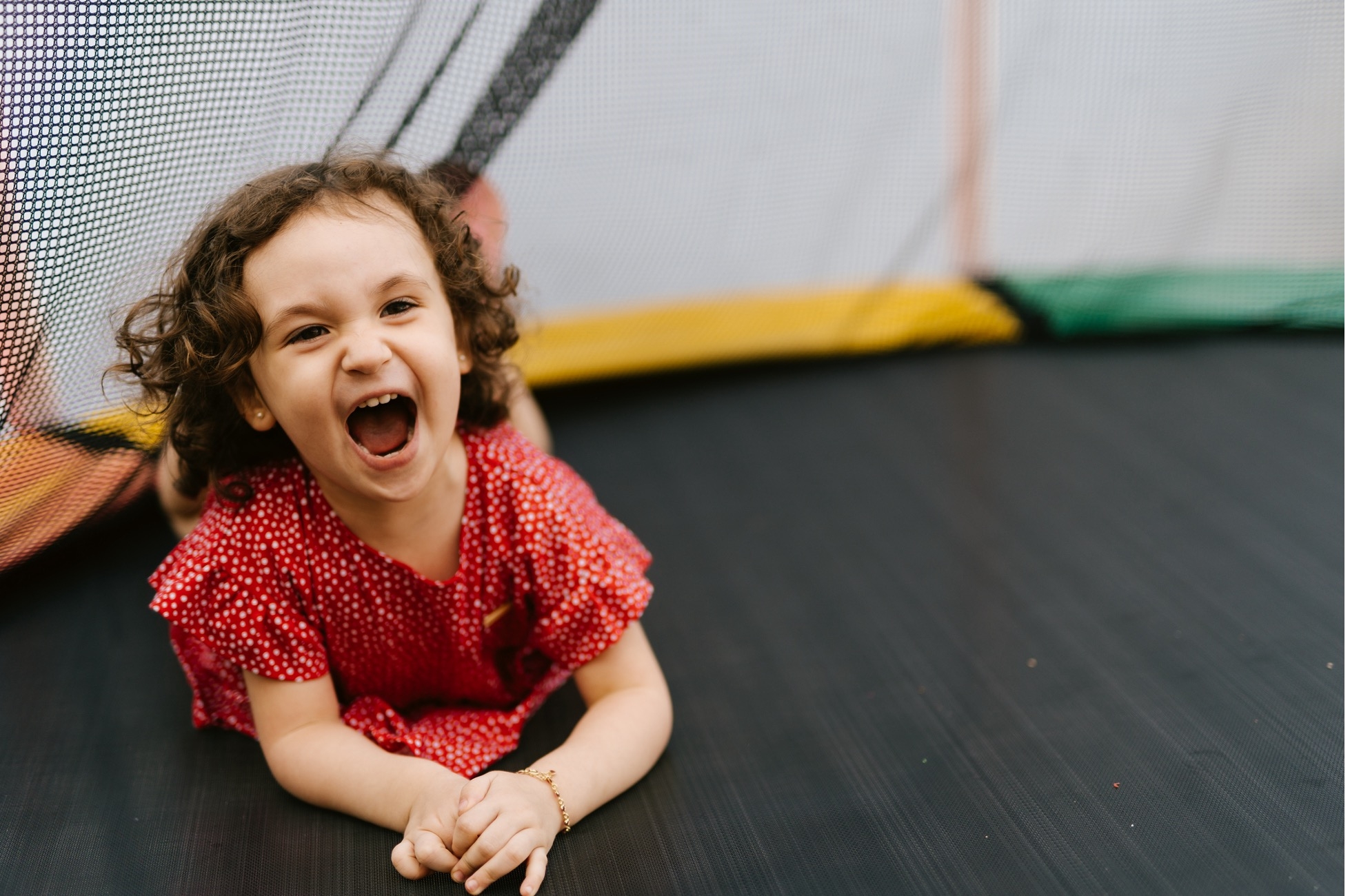 Young girl on a backyard trampoline with safety netting, mid-air, smiling, unaware of the potential injury risks highlighted by ER. 