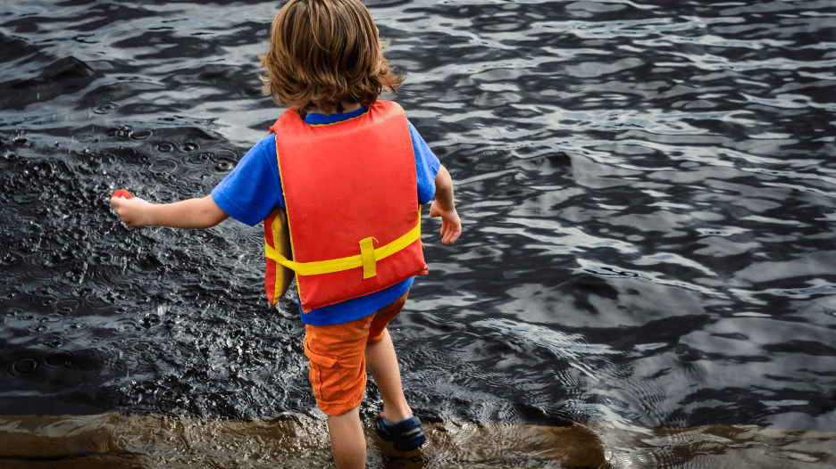 Child wearing a life jacket stepping into a lake, demonstrating water safety for kids