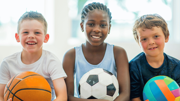 Happy kids with basketball, soccer ball, and volleyball ready for sports season after getting sports physicals