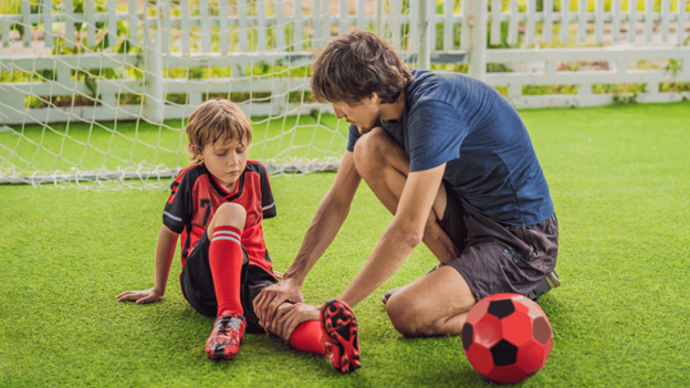 Young soccer player with acute fracture injury being helped by coach on soccer field