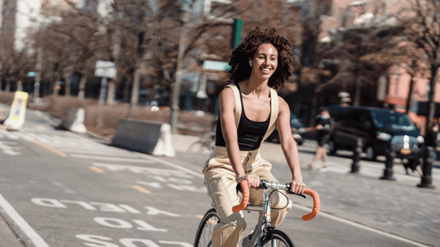 Young woman riding bicycle safely in NYC bike lane wearing casual clothes and smiling