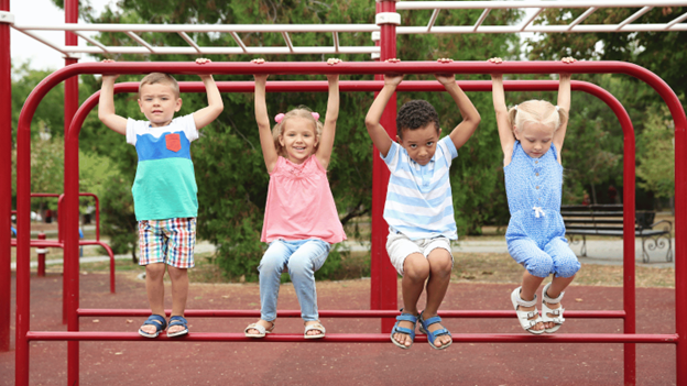Four children hanging from red monkey bars at a playground, demonstrating proper grip technique for playground safety