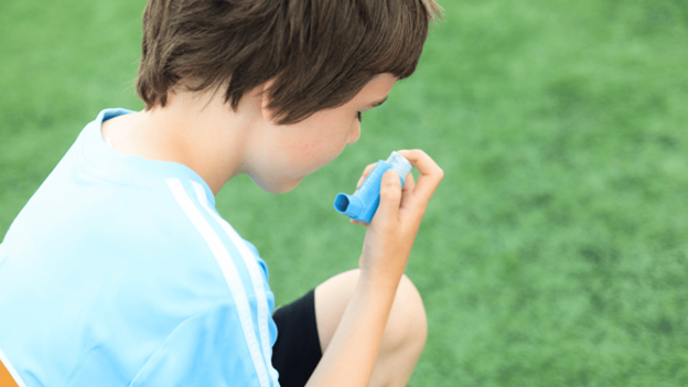 Young soccer player using an asthma inhaler on the field to manage exercise-induced asthma symptoms