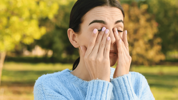 Woman outside rubbing her eyes from fall allergies