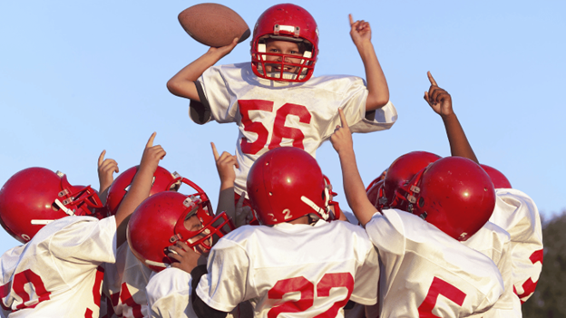 Youth football players in red helmets and uniforms celebrating together on the field 