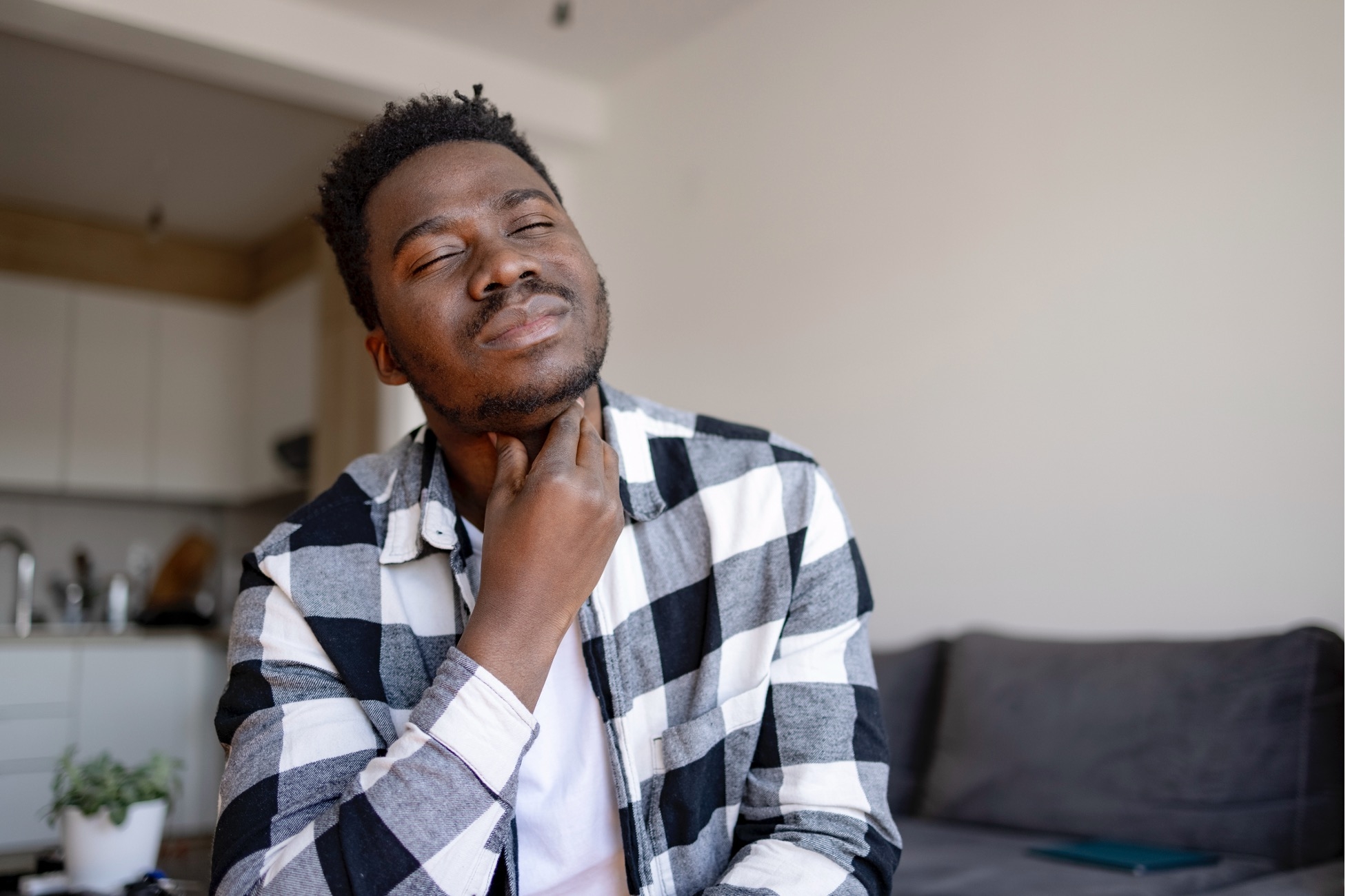 African American young man feeling ill at home, having a throat ache and feeling uncomfortable
