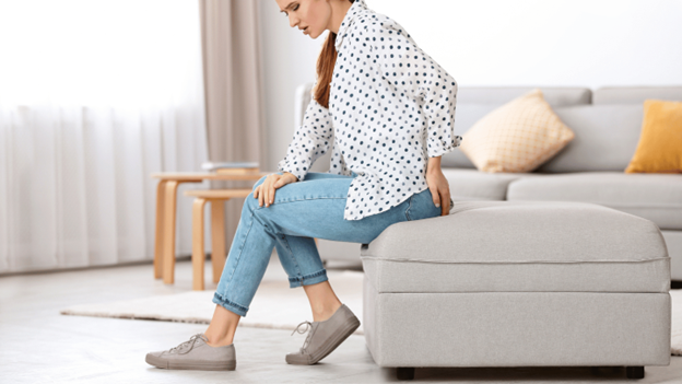 Woman experiencing hemorrhoid discomfort while sitting on the edge of a couch at home