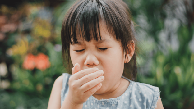 Young child coughing with hand over mouth outdoors